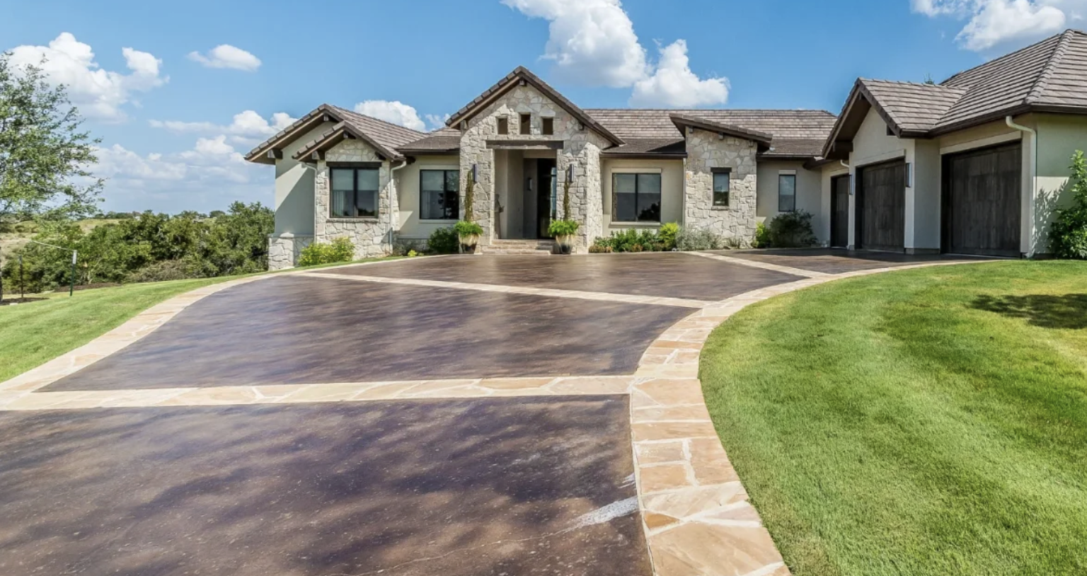 Acid-stained brown concrete driveway with tan flagstone border bands at a stone-front home in Ponte Vedra Beach, FL