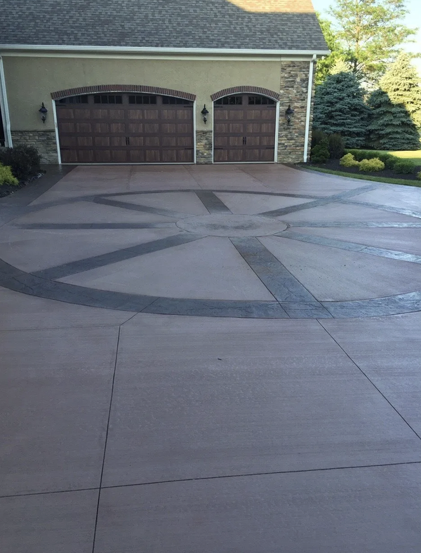 Colored concrete driveway with a charcoal stamped compass-wheel inlay in front of a two-car garage in Fleming Island, FL