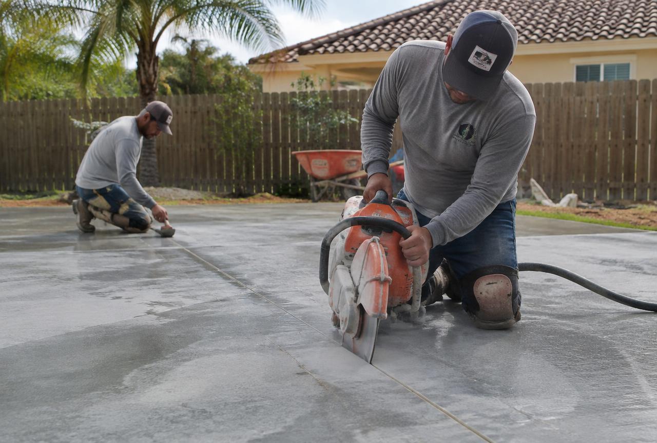 Concrete crew saw-cutting control joints into a fresh residential slab
